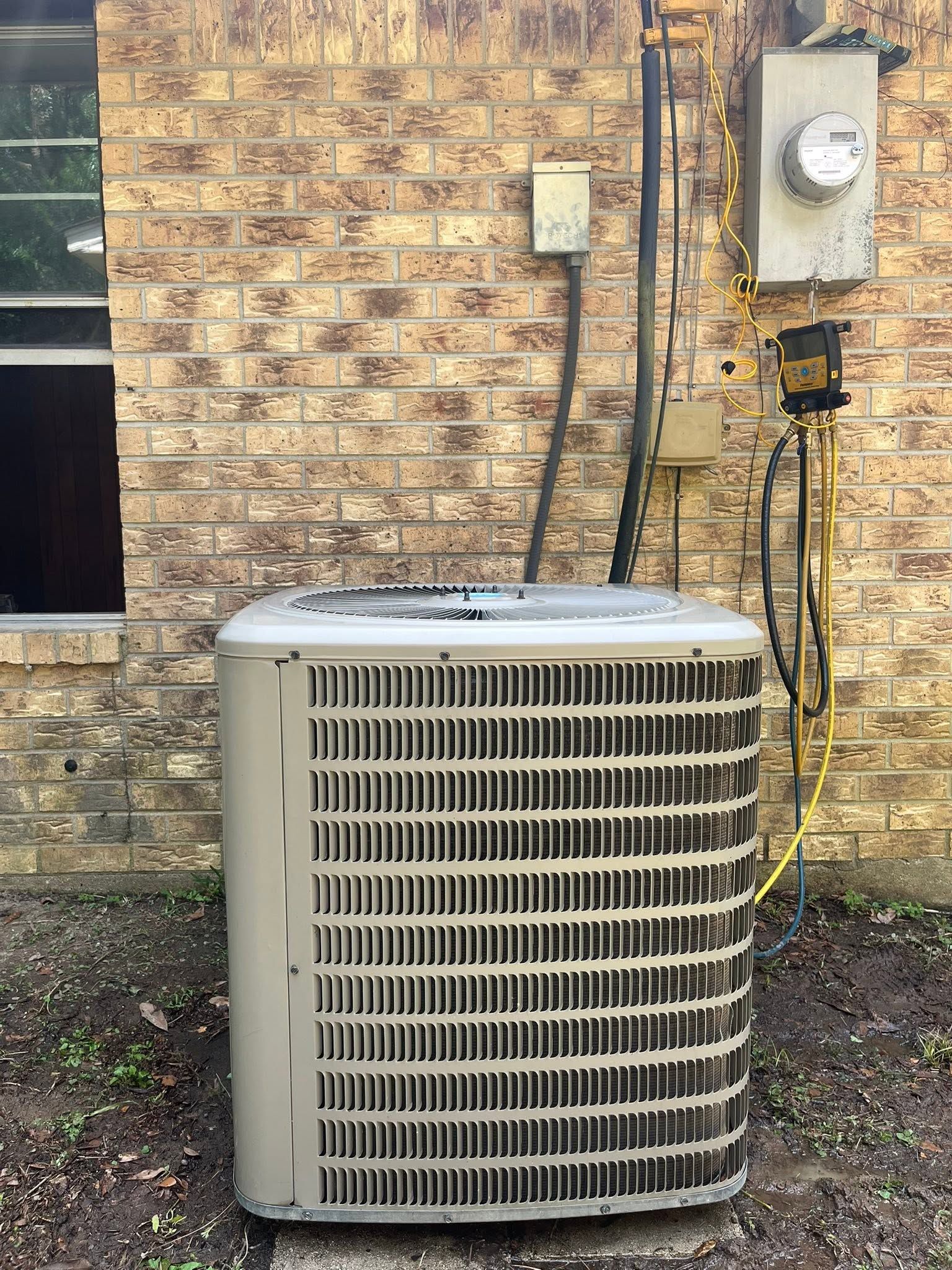 Outdoor air conditioner unit beside a brick wall and utility meter.
