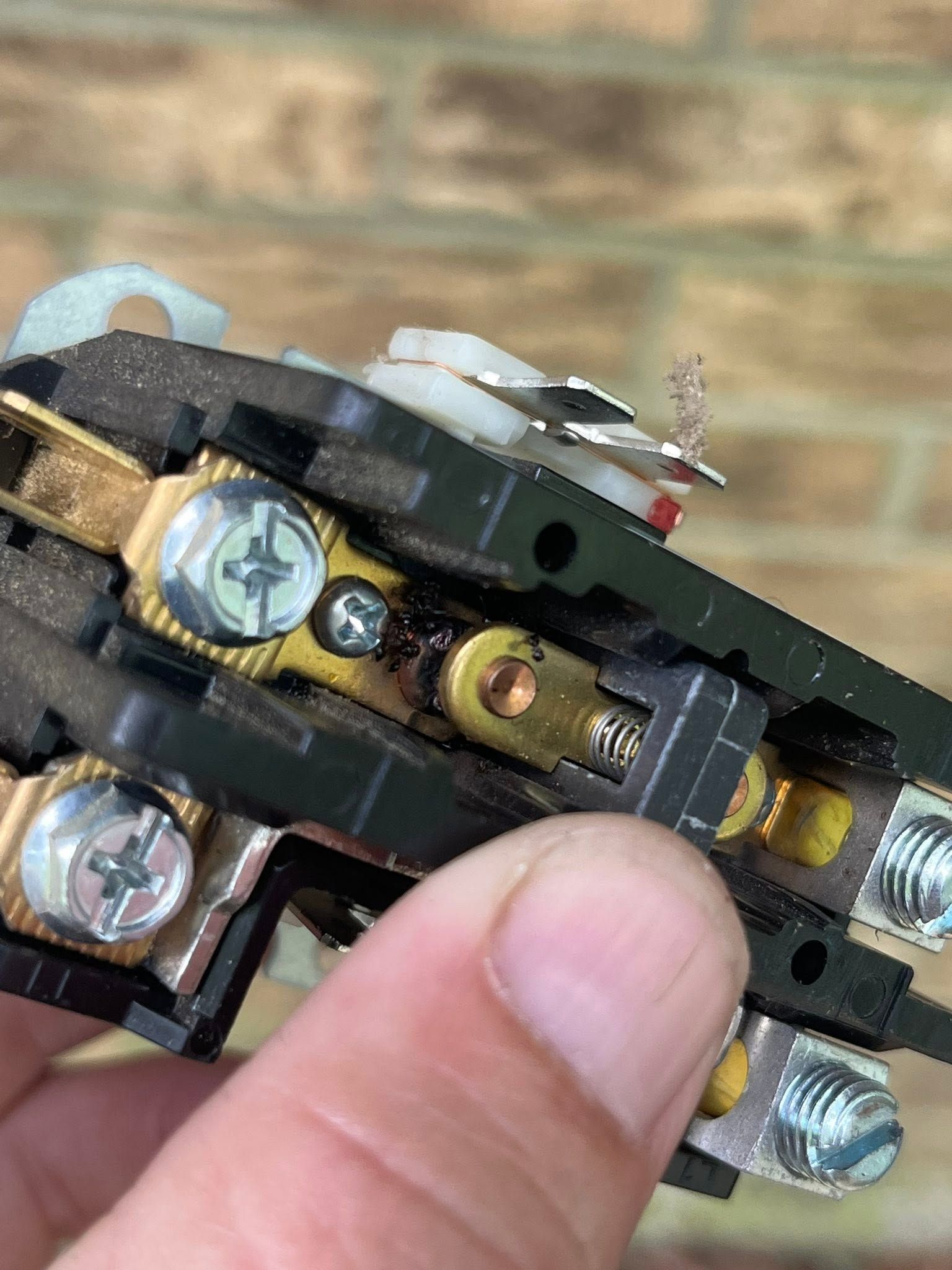 Close-up of a finger adjusting metal electrical switch contacts with screws and brass parts
