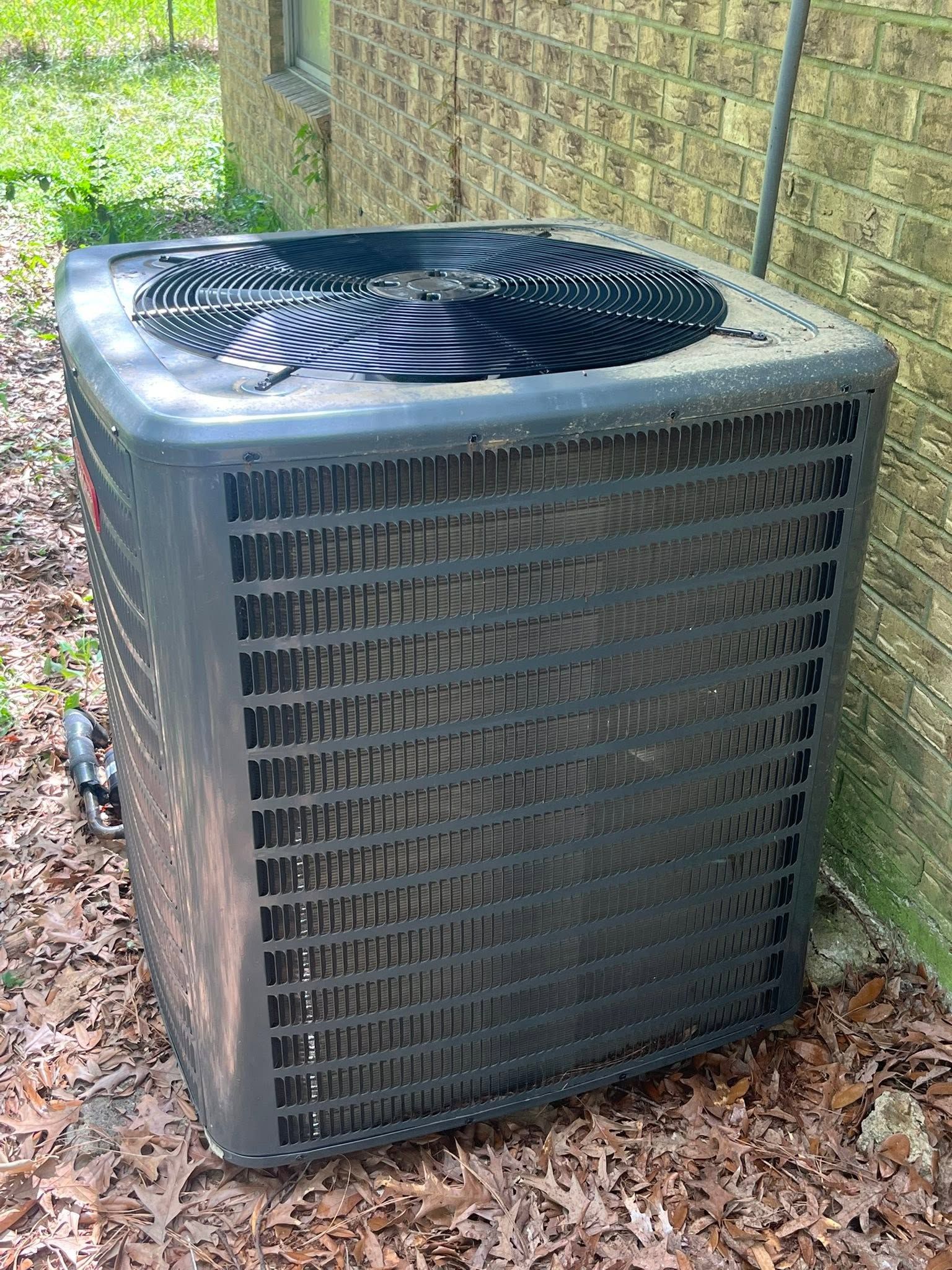 Outdoor air conditioner unit beside a chain-link fence, with a damaged top fan grille