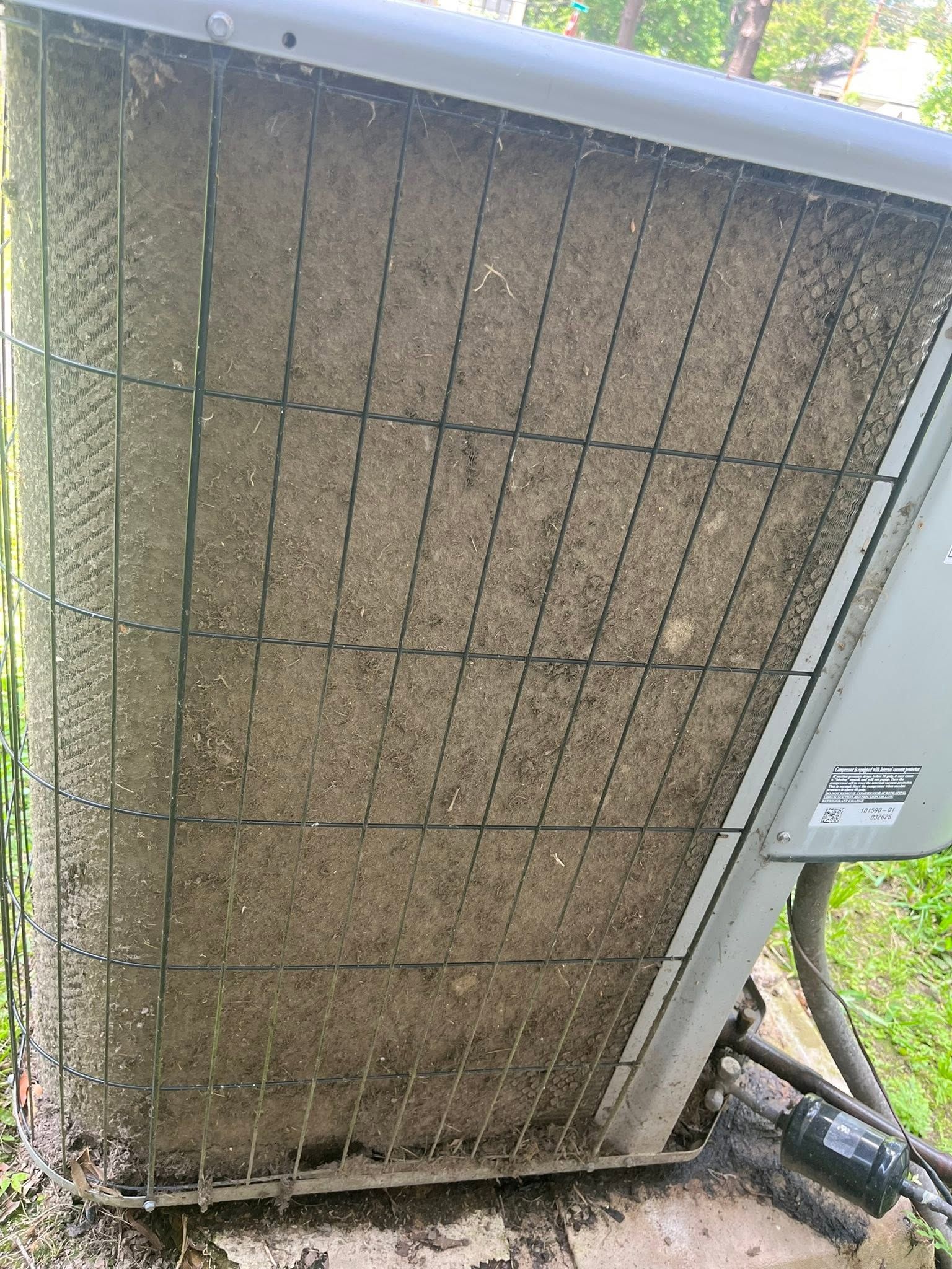 Close-up of a dusty outdoor HVAC unit with a metal vent panel and pipes beside a wall.