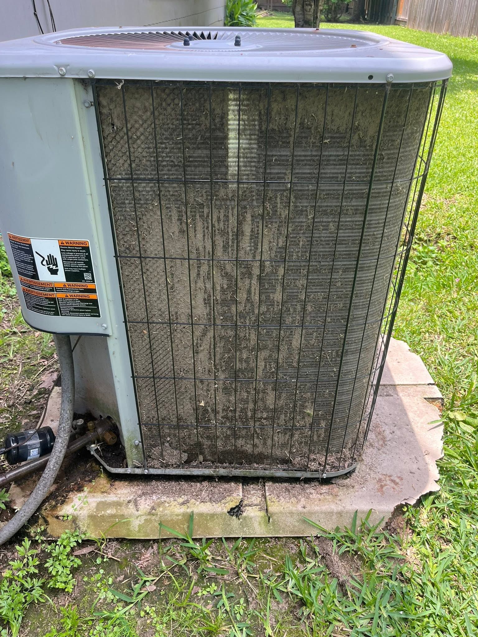 Outdoor air conditioner condenser unit with a dirty, clogged front grille on a concrete pad.