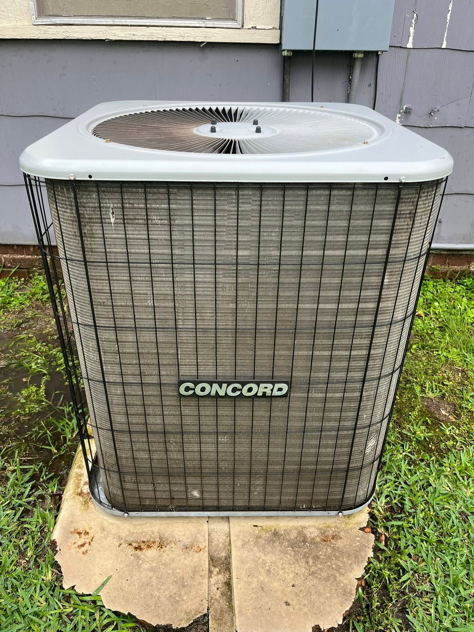 Outdoor Concord air conditioner unit on a concrete pad beside a building wall.
