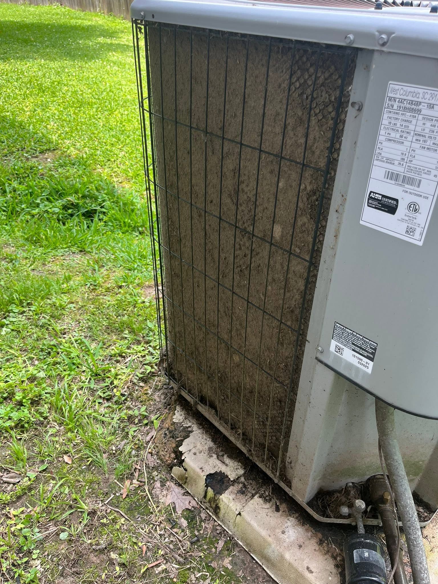 Outdoor air conditioner unit with dirty, clogged front coil beside a grassy yard