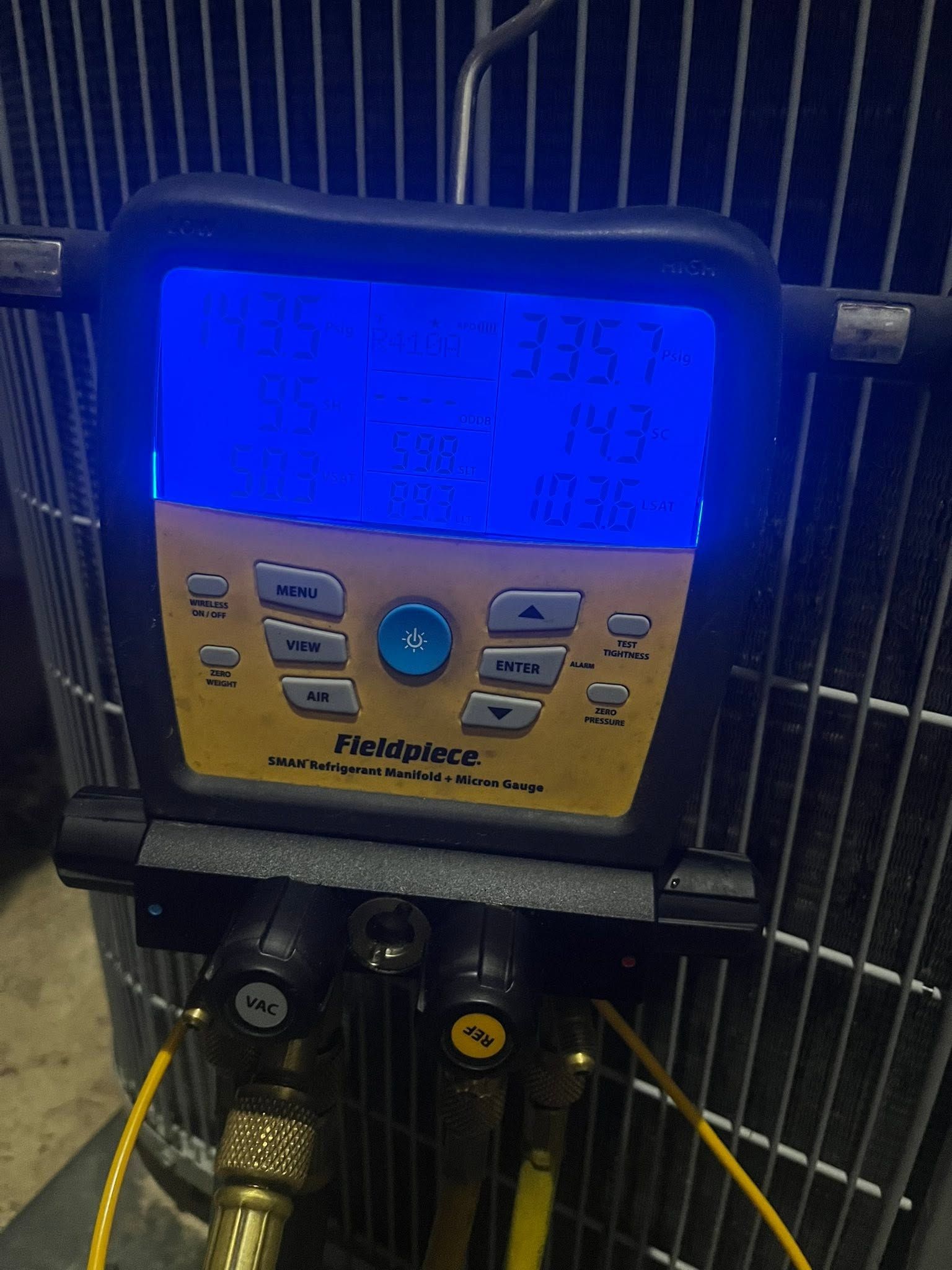 Blue irrigation controller with tan keypad mounted on a metal fence, with hoses below.