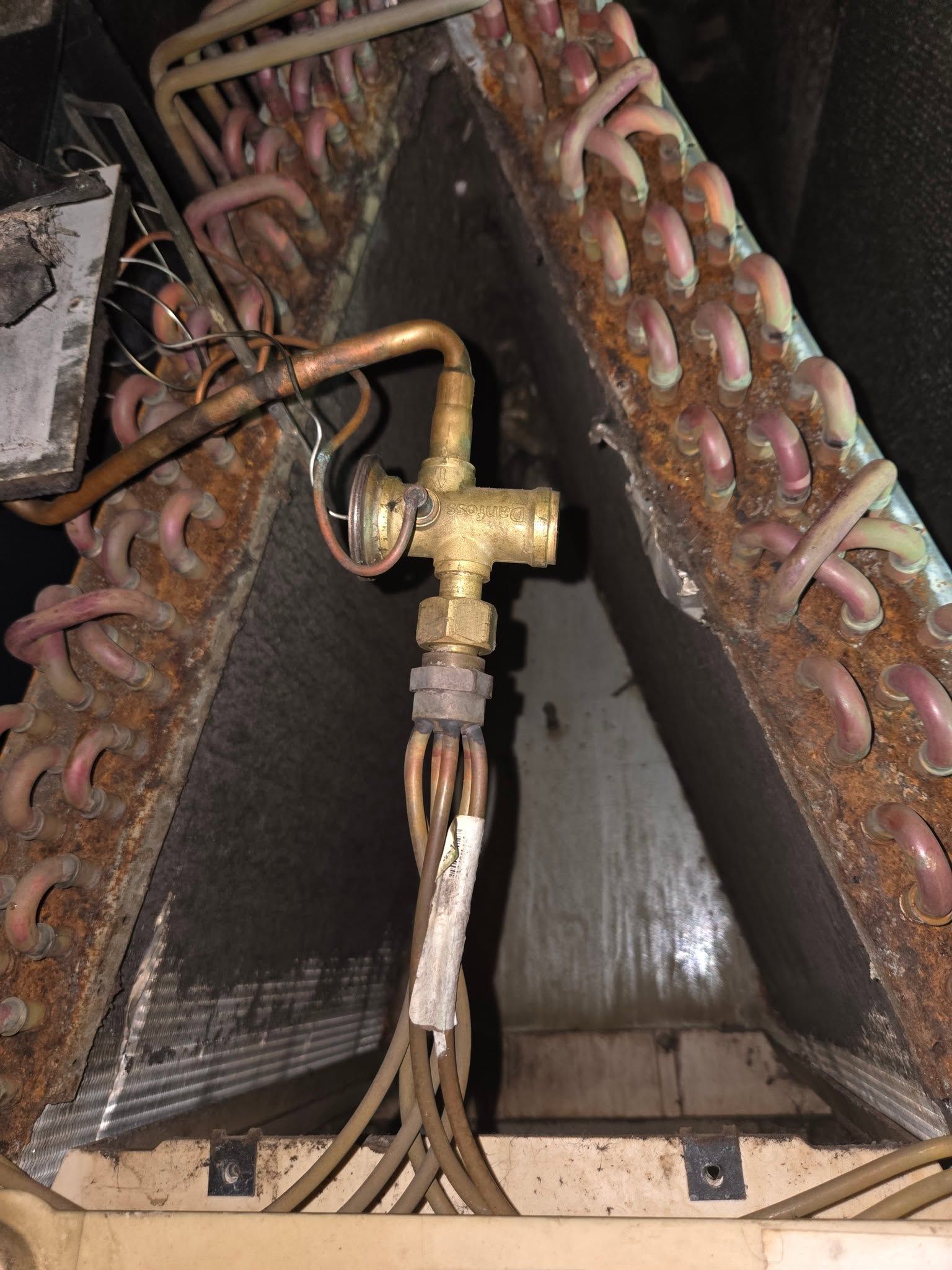 Close-up of a brass valve and copper tubing inside a dark mechanical unit with coiled components on both sides