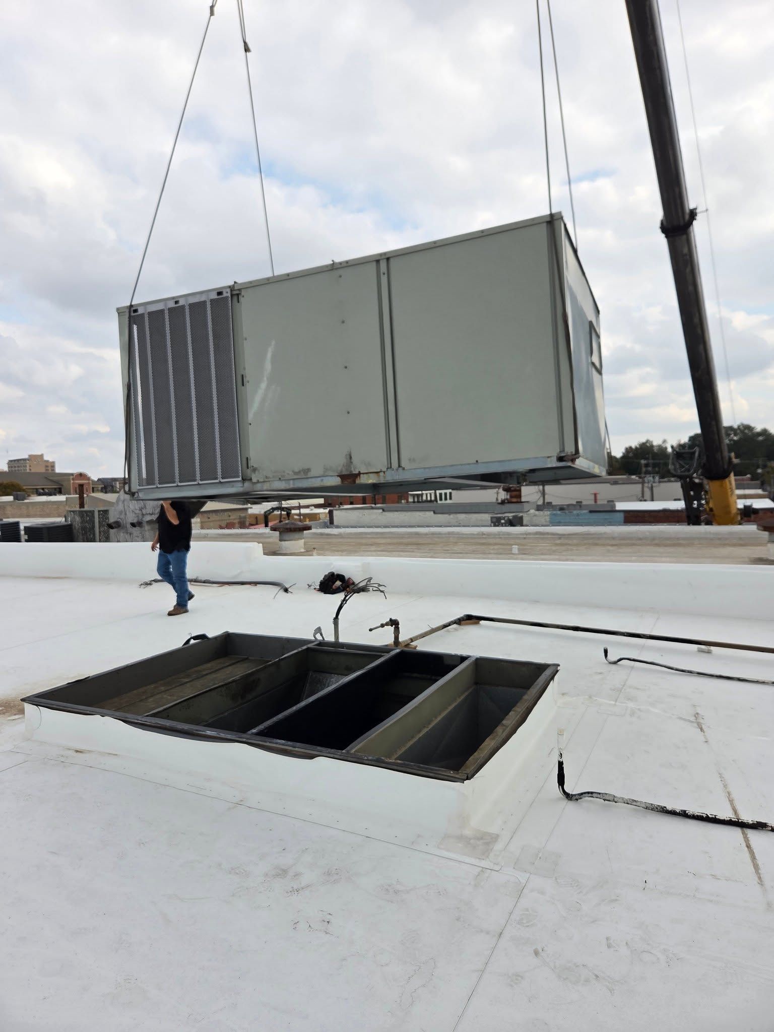 Crane lifting a large gray HVAC unit onto a white rooftop near open vents.