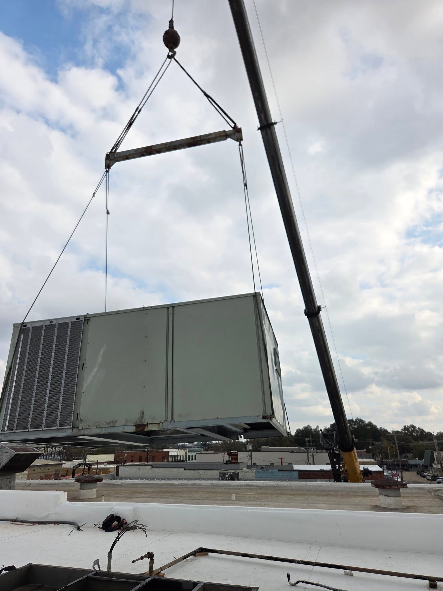 Crane lifting a large gray shipping container on a rooftop under a cloudy sky