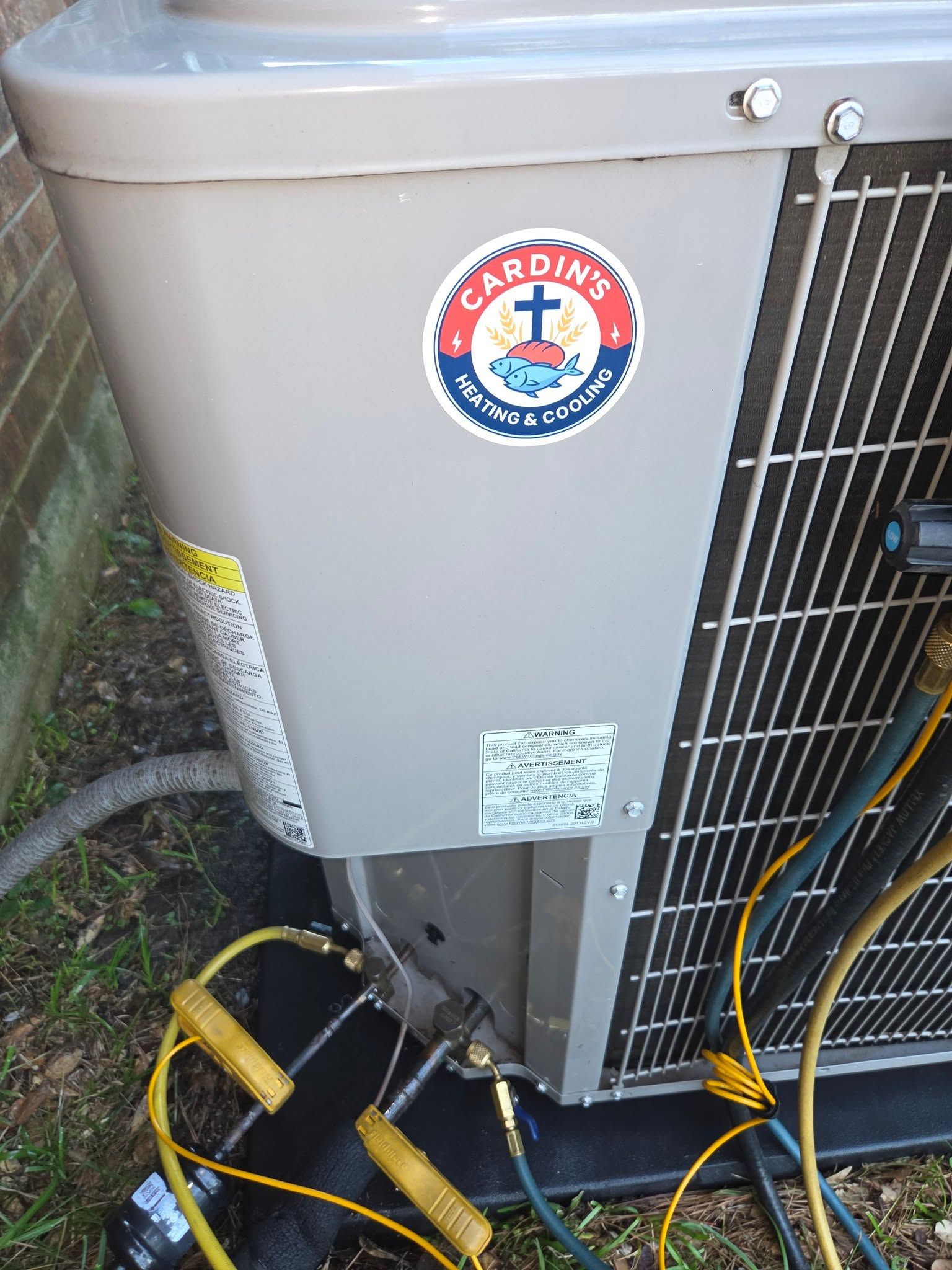 Outdoor air conditioner unit with hoses and wiring attached, showing a Cardinal logo on the front.