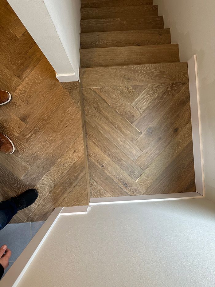 A person is standing next to a wooden staircase with a herringbone pattern.
