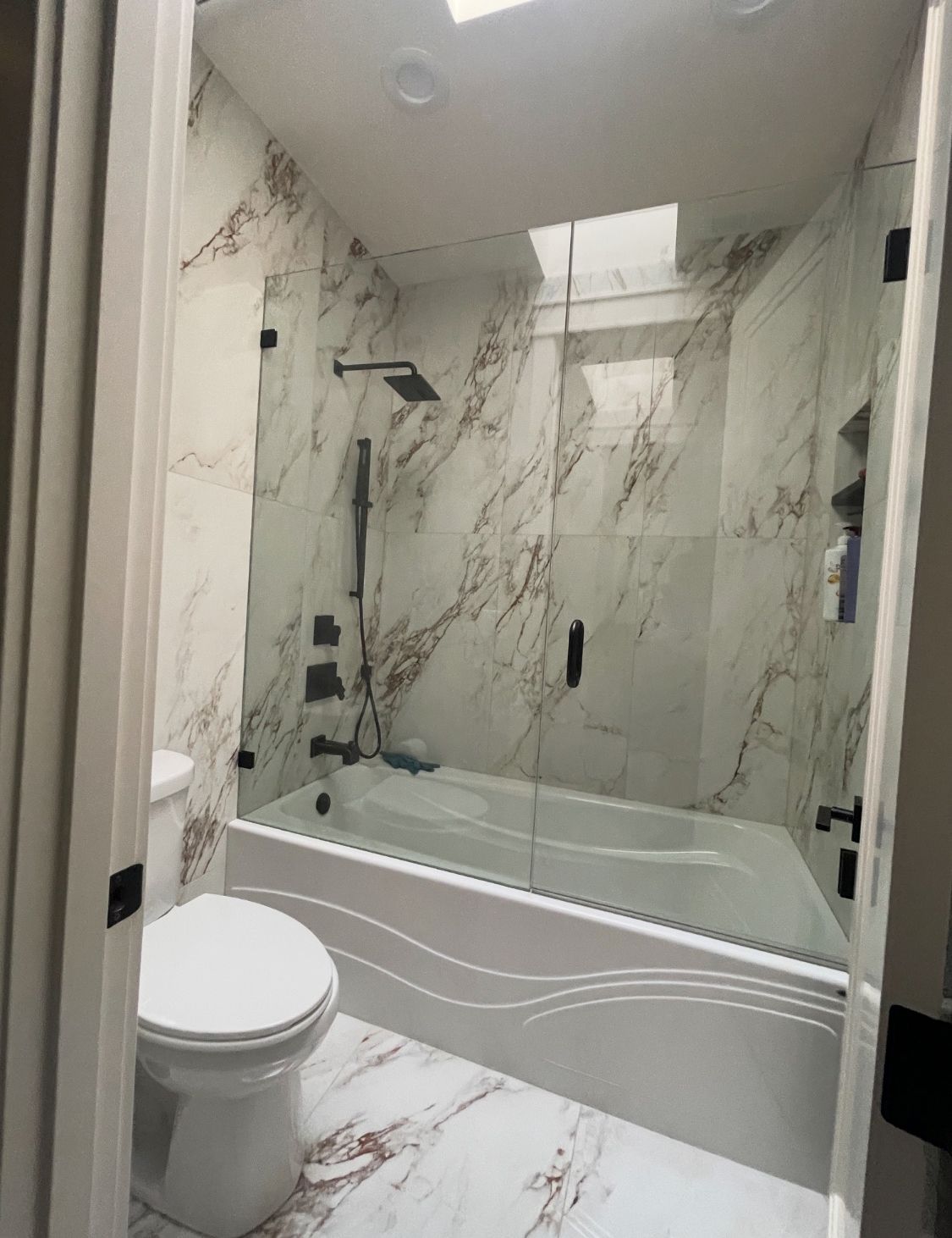 A bathroom with a toilet , tub , shower and marble walls.