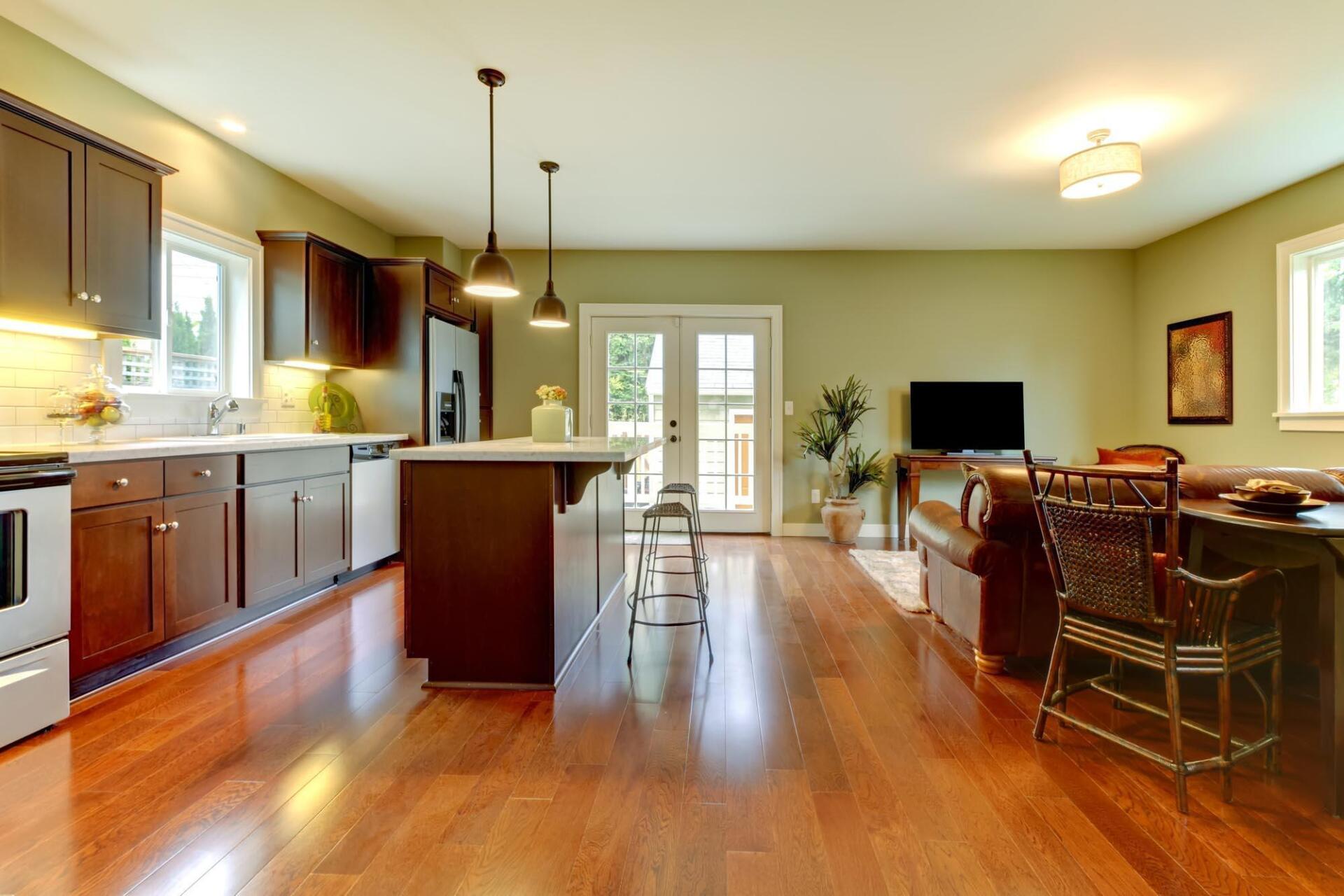 A kitchen and living room in a house with hardwood floors and green walls.