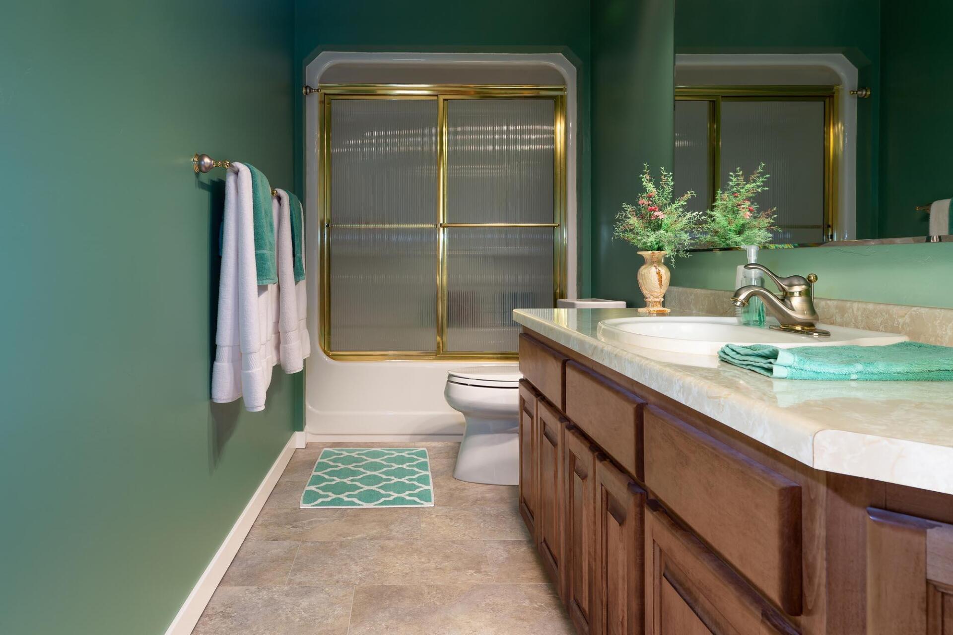 A bathroom with green walls , a toilet , sink , and shower.