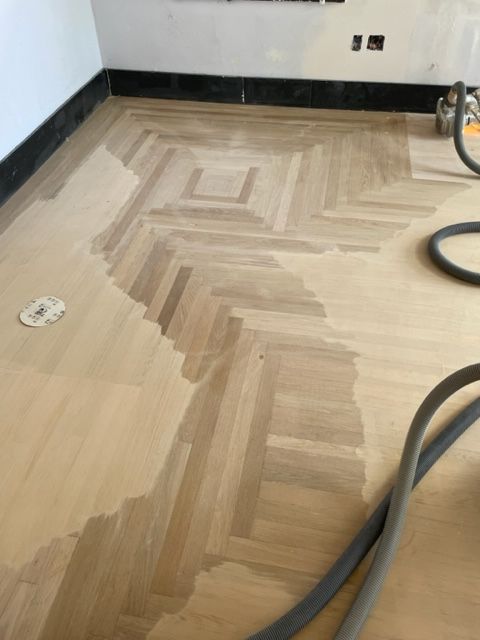 A wooden floor is being painted in a herringbone pattern