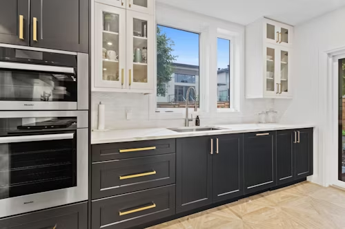 Modern kitchen with dark gray cabinets, white countertops, and gold hardware.