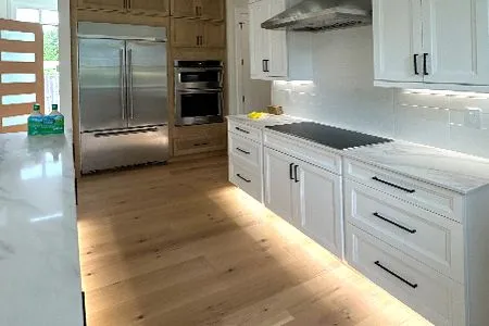 Modern bright kitchen with white cabinets, stainless steel appliances, and light wood floors