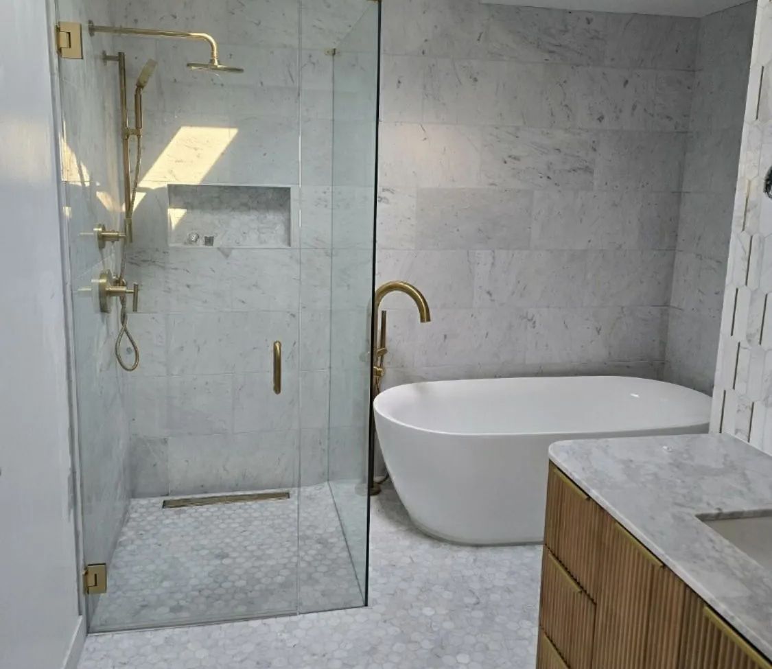 Modern bathroom with a glass shower, a white bathtub, and gold fixtures.