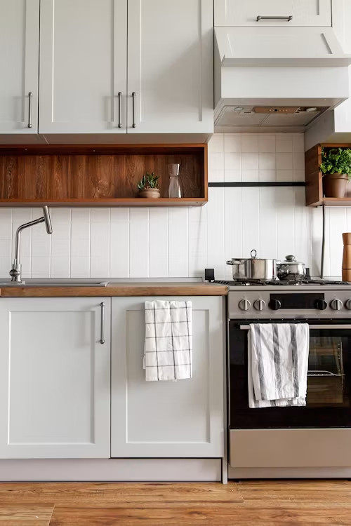 Bright white kitchen with wood accents, stainless stove, and a towel hanging on the oven handle.