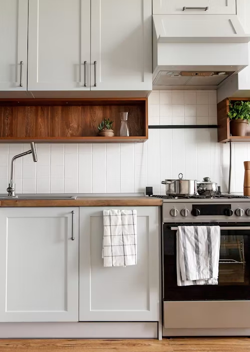 Modern white kitchen with wood shelves, stainless stove, and hanging dish towels