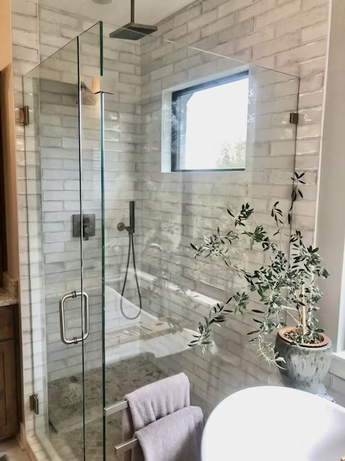 Glass shower with white subway tiles, handheld showerhead, window, and striped towels on a stool