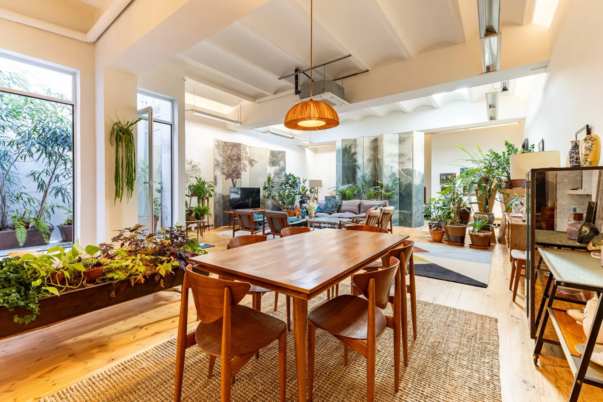 Salón comedor con cocina abierta, techos altos, vigas vistas, mobiliario de madera y alfombras naturales en vivienda reformada.
