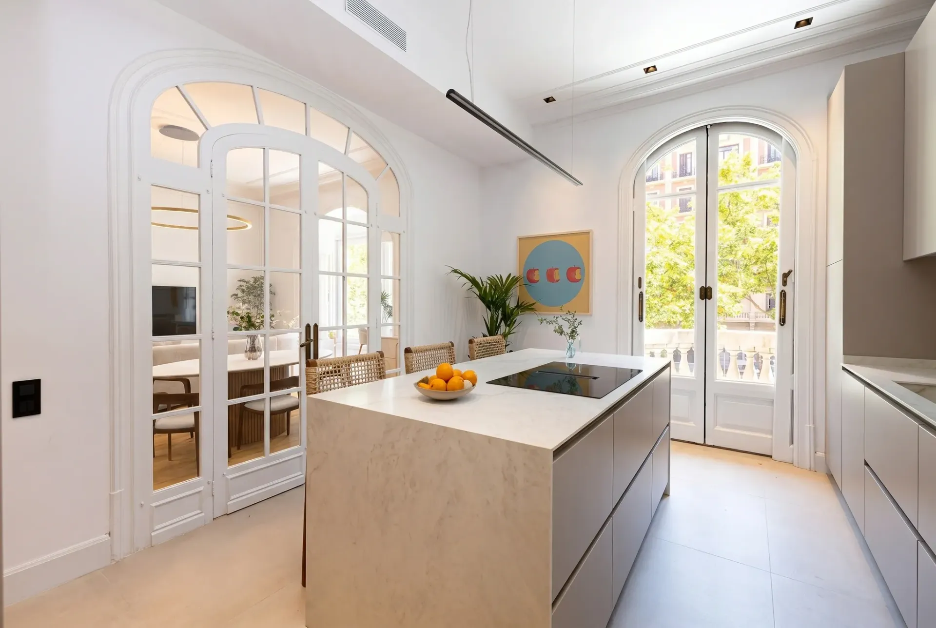Render inmobiliario de cocina luminosa con isla central, ventanales arqueados y salida a balcón