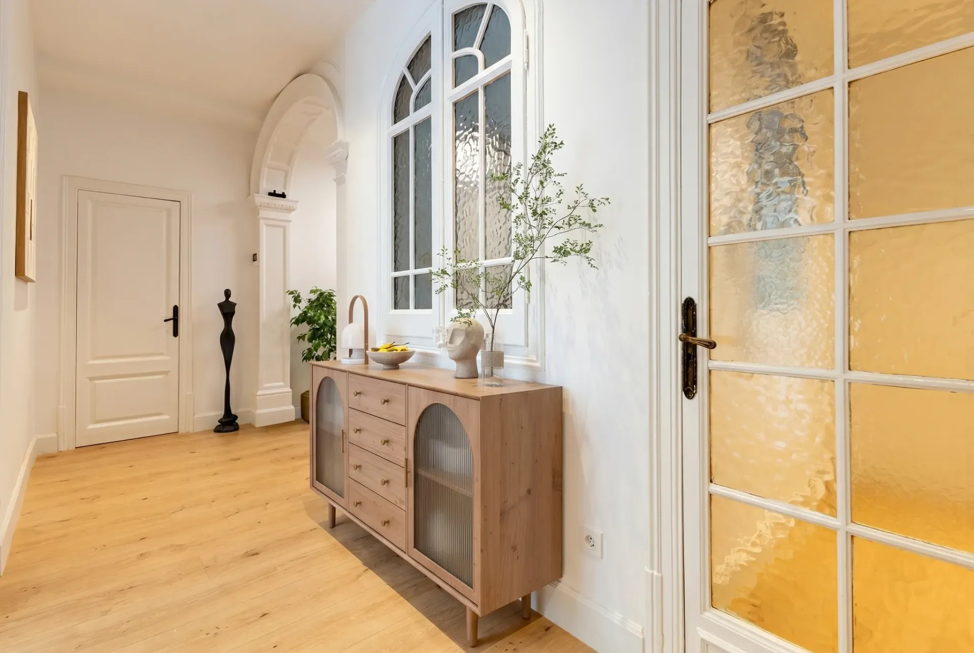 Render inmobiliario de recibidor luminoso con ventanales de arco y aparador de madera