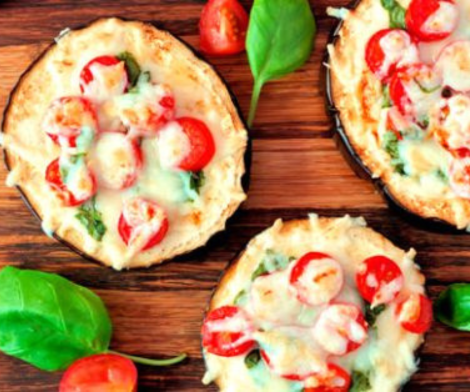 Drie gebakken aubergineschijven, bedekt met gesmolten kaas, cherrytomaatjes en verse basilicumblaadjes, geserveerd op een houten ondergrond.
