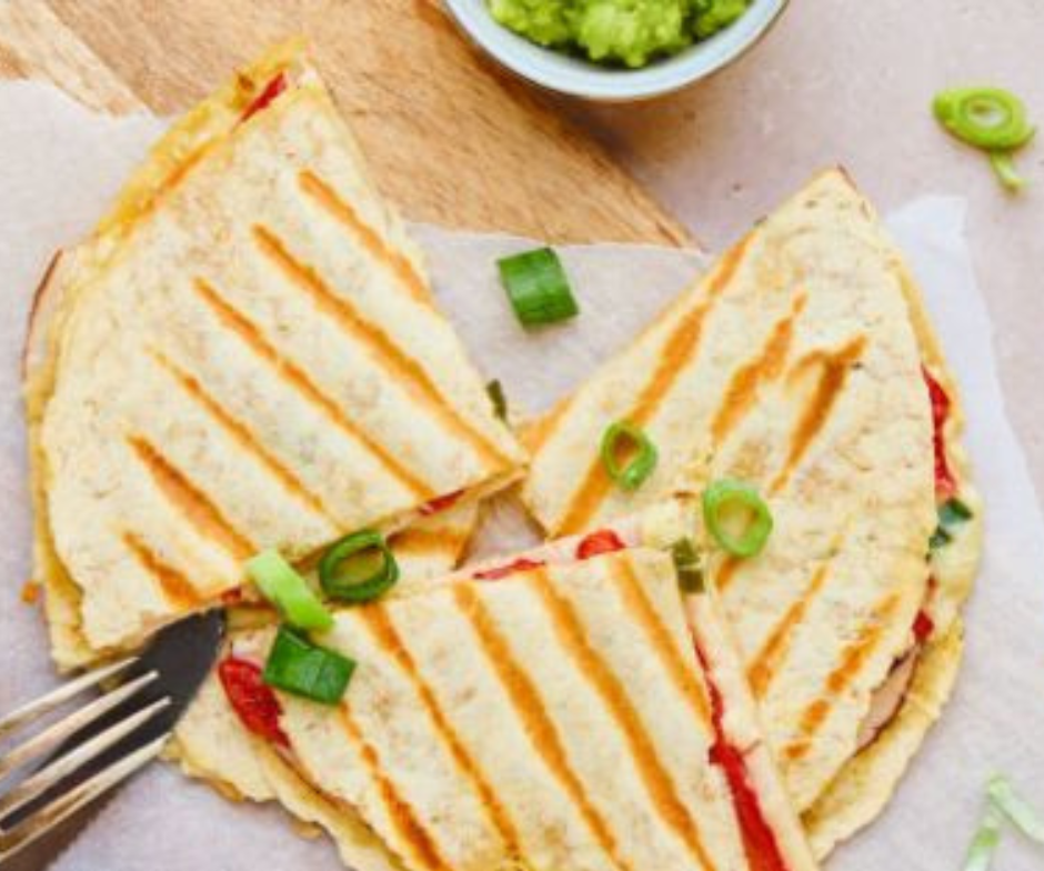 Gegrilde tortillaquesadilla's, in driehoekjes gesneden en gegarneerd met lente-uitjes, met een portie guacamole erbij.