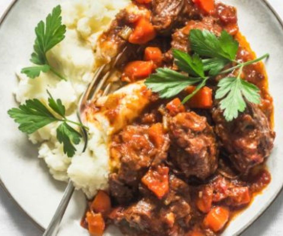 Een stevige runderstoofpot met wortelen in een rijke, donkere saus, geserveerd met romige aardappelpuree en gegarneerd met peterselie.