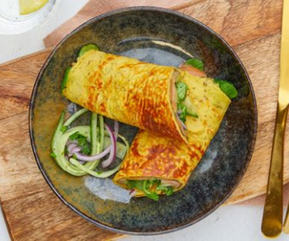 Twee goudbruine crêpes gevuld met groenten, geserveerd in een donkere kom met een salade van komkommer en rode ui.