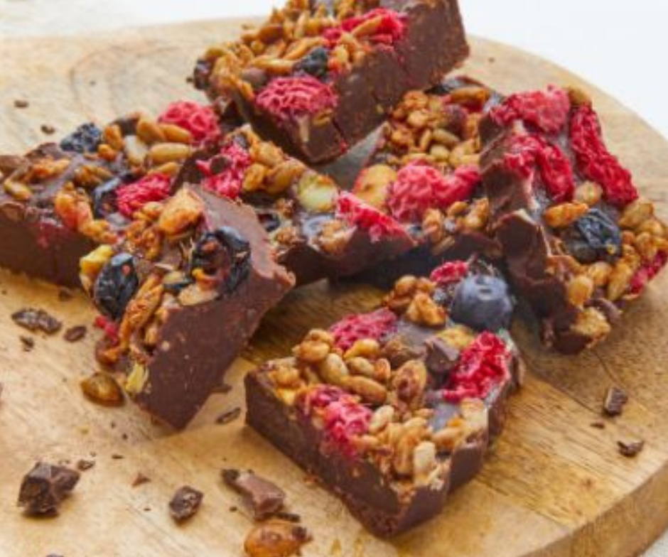Verschillende stukken pure chocoladefudge, bedekt met gepofte granen, gedroogde frambozen en bosbessen, op een houten plank.