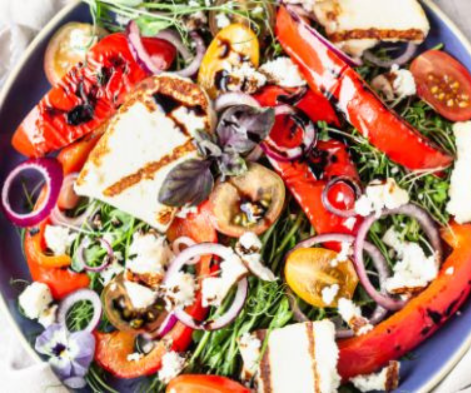 Een kleurrijke salade met gegrilde halloumi, geroosterde rode paprika's, cherrytomaten, rode ui en verse bladgroenten met dressing.