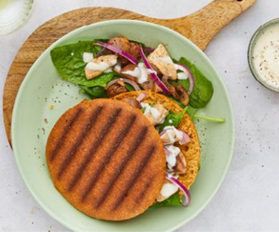 Een gegrilde platbroodsandwich met kip, spinazie en rode ui op een lichtgroen bord, geserveerd met een dressing.
