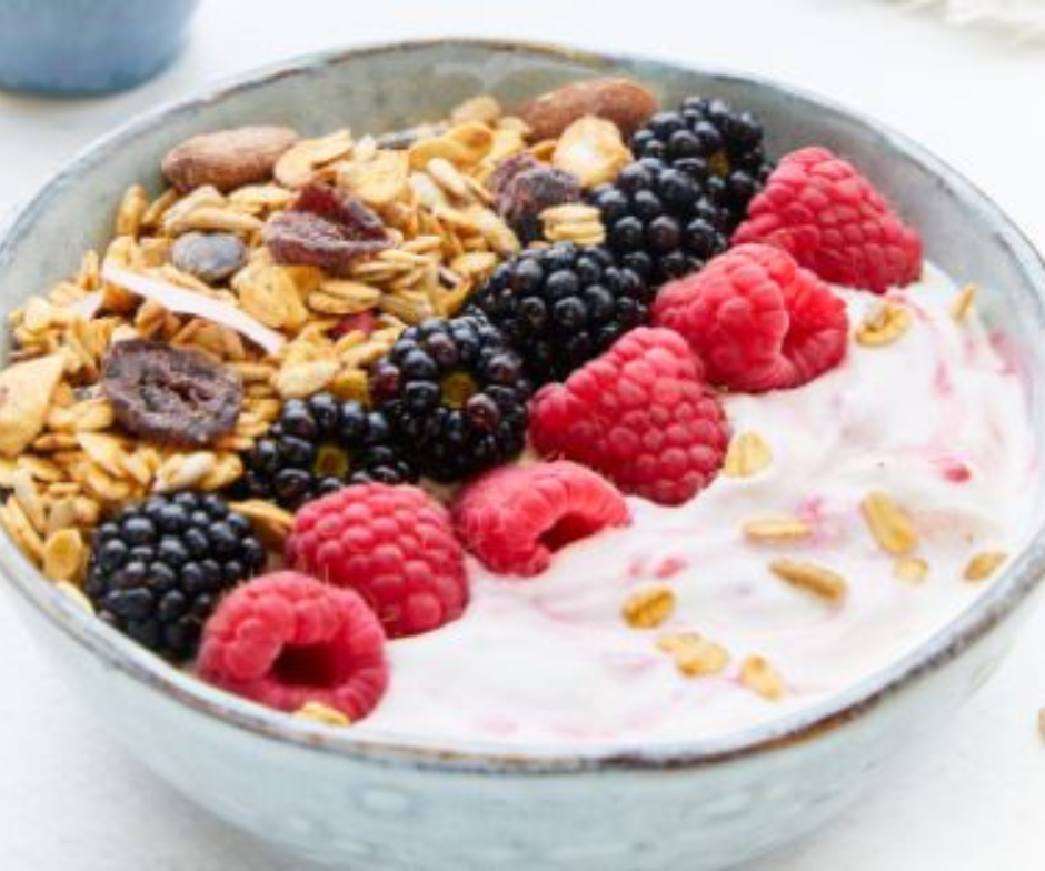 Een kom yoghurt met daarop granola, frambozen en bramen, in diagonale rijen gerangschikt.