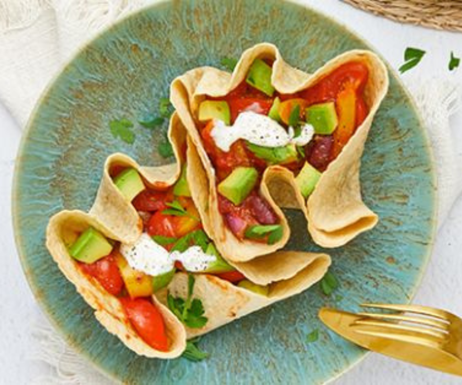 Twee opgevouwen tortilla's gevuld met rode bonen, tomaten, avocado en een klodder witte saus op een turquoise bord met textuur.