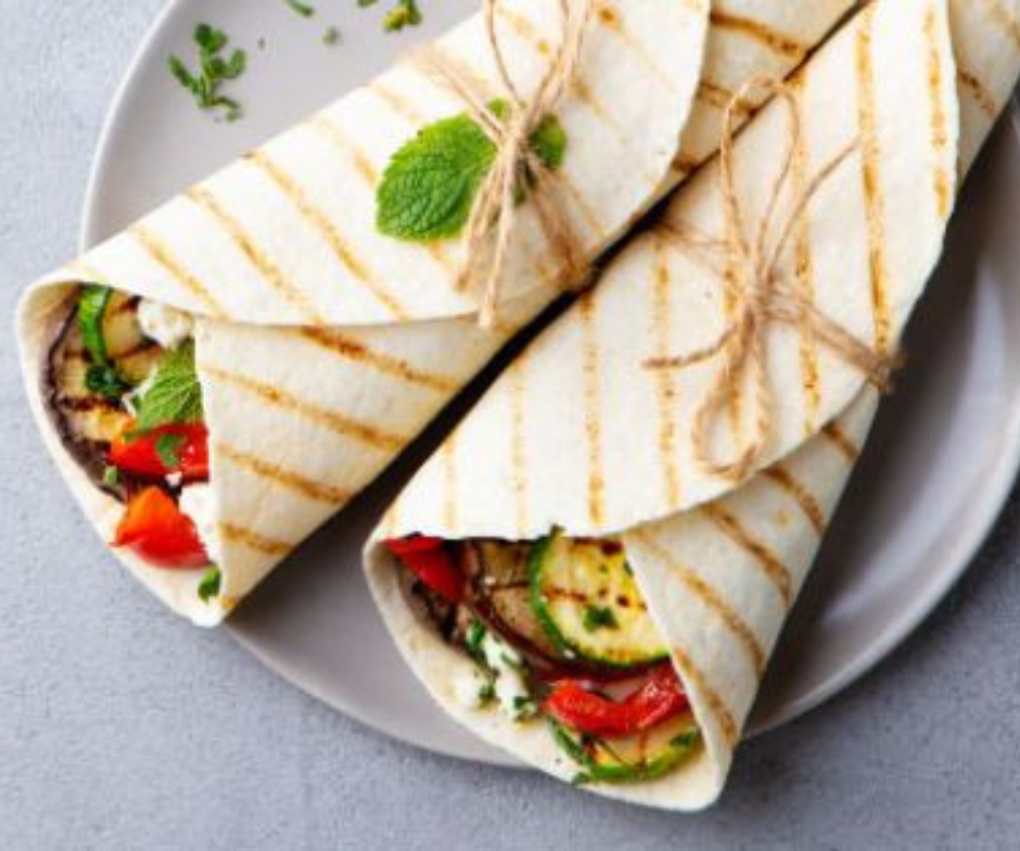 Twee gegrilde groentewraps, gegarneerd met verse munt en vastgebonden met keukentouw, op een grijs bord.