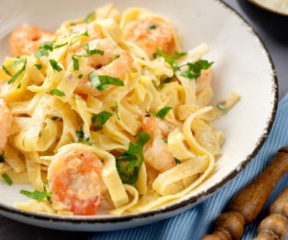 Een kom garnalenfettuccine, overgoten met een romige witte saus en gegarneerd met verse groene kruiden.