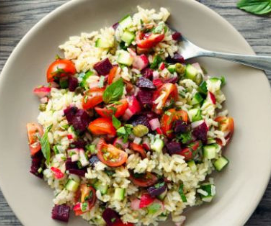 Een beige bord gevuld met een rijstsalade met rode cherrytomaatjes, blokjes rode biet, groene komkommer en verse basilicumblaadjes.