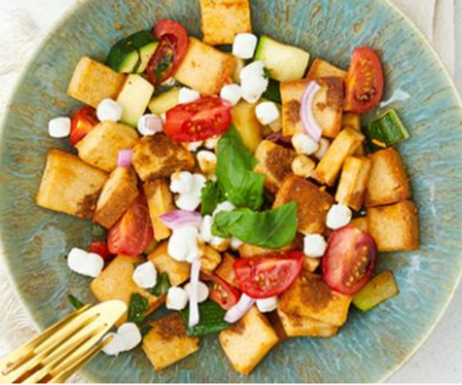 Een kom salade van gebakken gnocchi met cherrytomaatjes, komkommer, rode ui, witte kaas en verse basilicum.