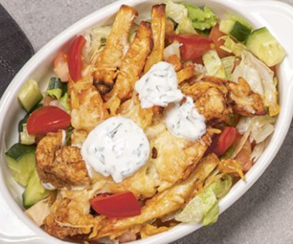 Een witte ovale kom gevuld met een salade van sla, komkommer en tomaat, gegarneerd met gefrituurde kip, kaas en kruidensaus.