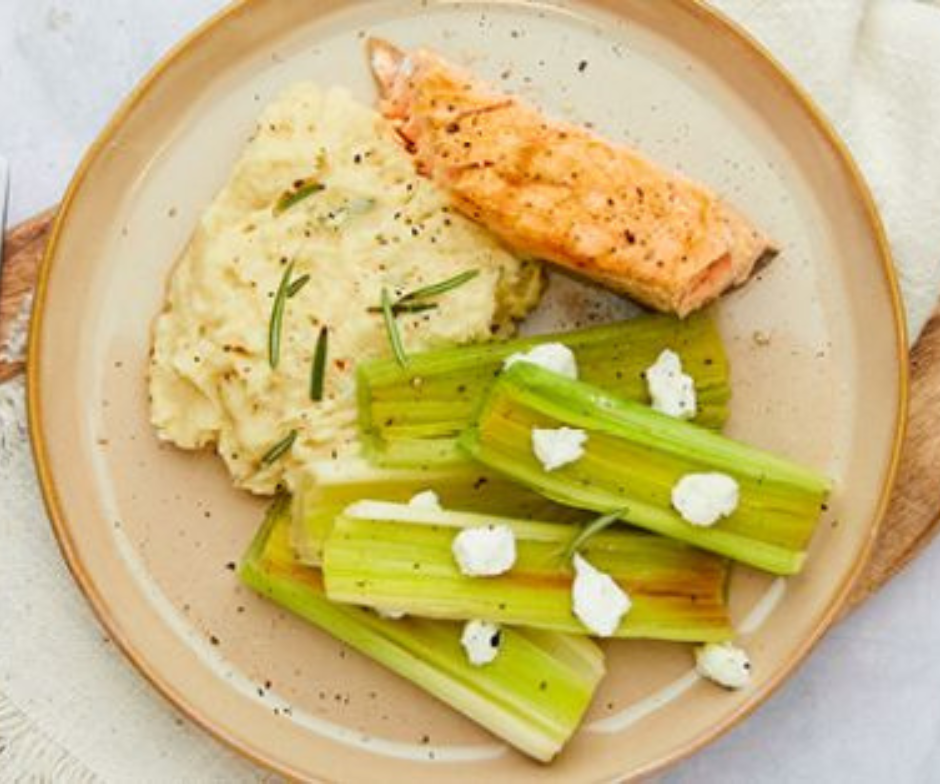 Een dinerbord met gebakken zalm, romige aardappelpuree met rozemarijn en gebakken prei, gegarneerd met geitenkaas.
