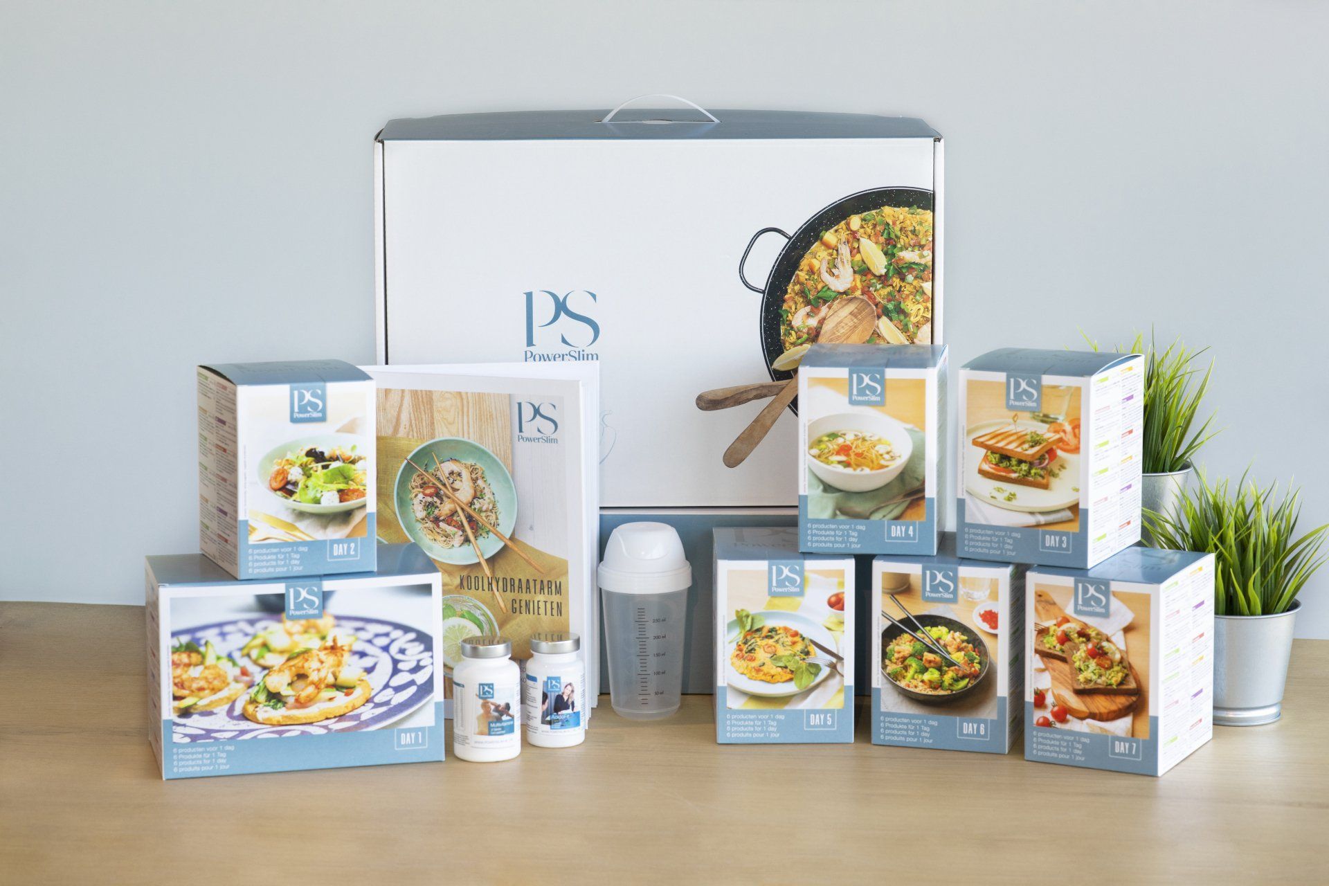 Een afslankpakket van het merk PS met diverse voedingsproducten, twee flesjes supplementen, een shaker en een grote presentatiedoos.
