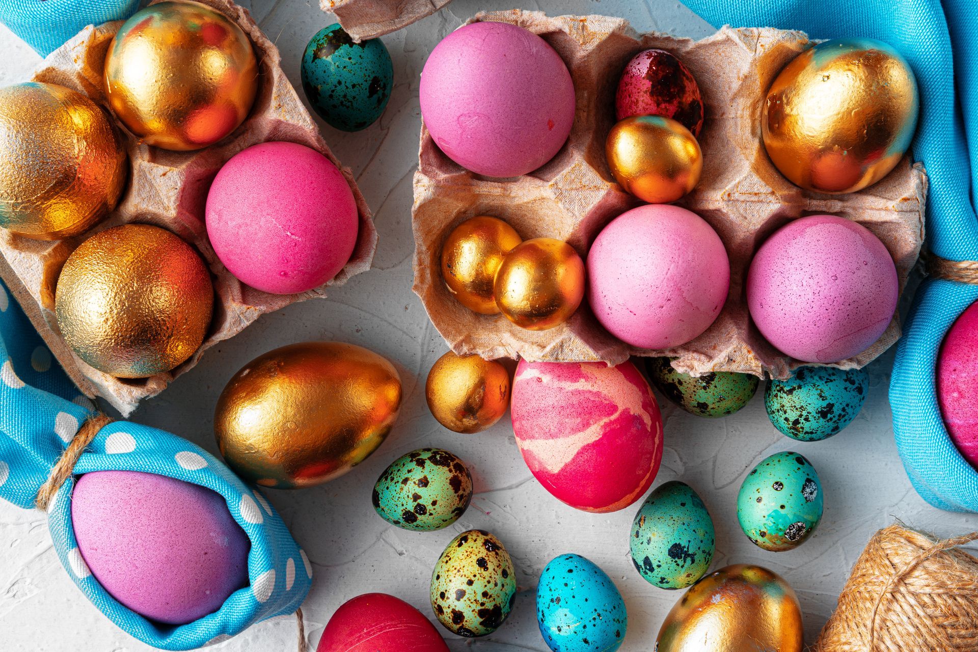 Een verzameling gouden, roze en gespikkelde blauwe paaseieren, gerangschikt in kartonnen doosjes en verspreid over een witte ondergrond.