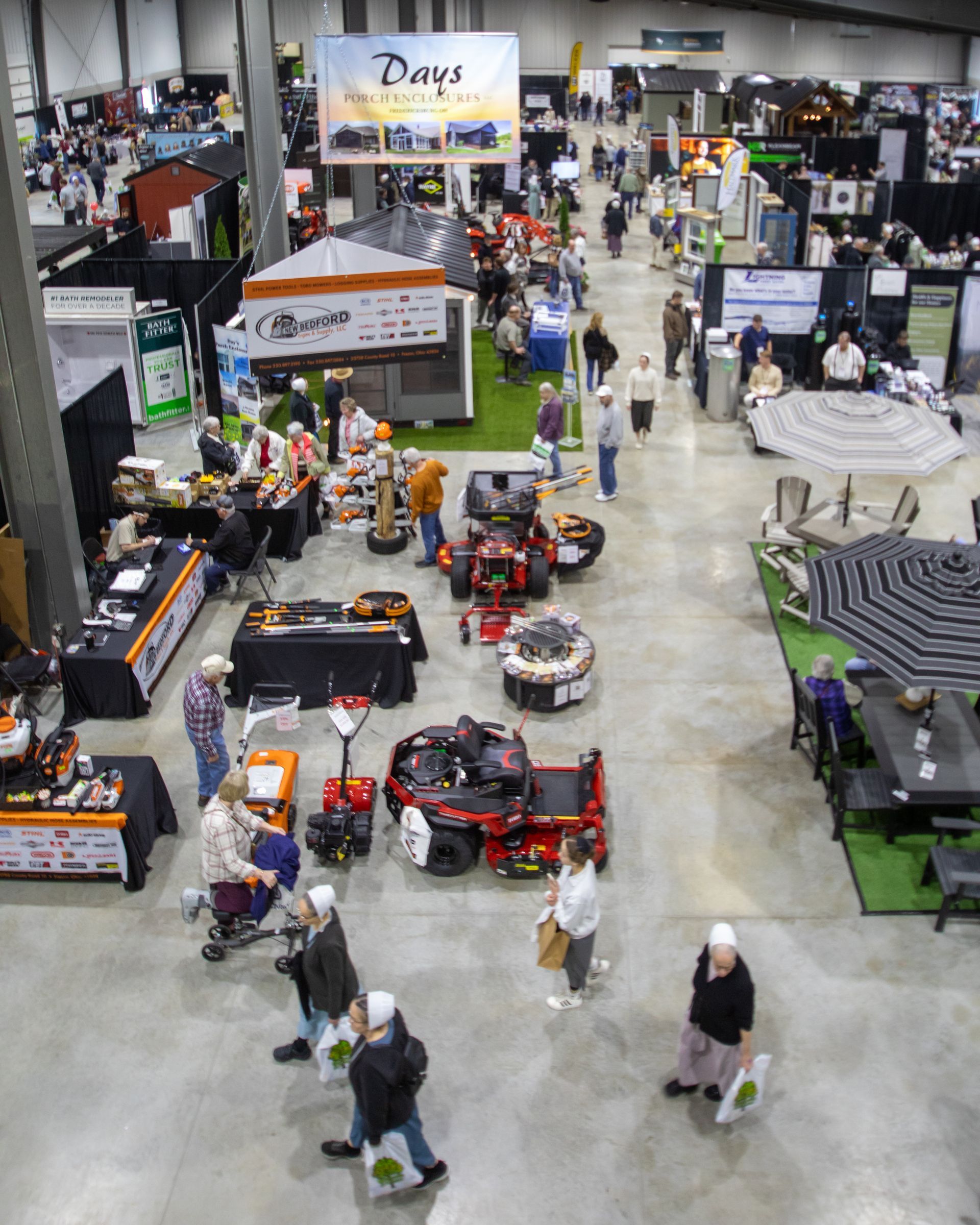 People browsing booths at an indoor trade show with sheds and products on display.