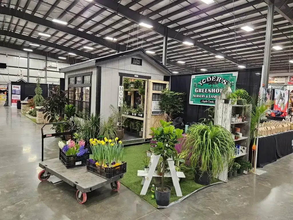 A garden shed display with plants and flowers inside an industrial building.