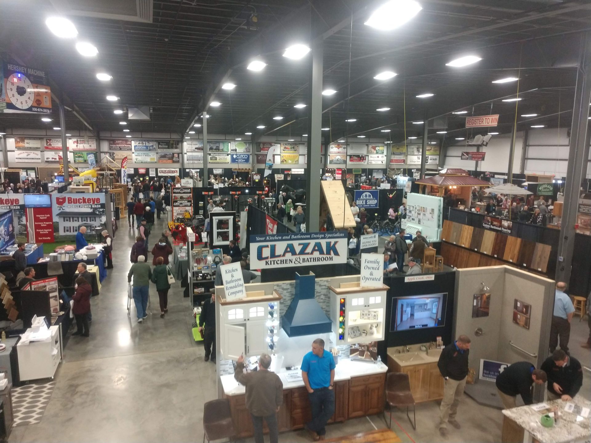 Large interior view of a trade show with booths, people walking, and overhead lights.