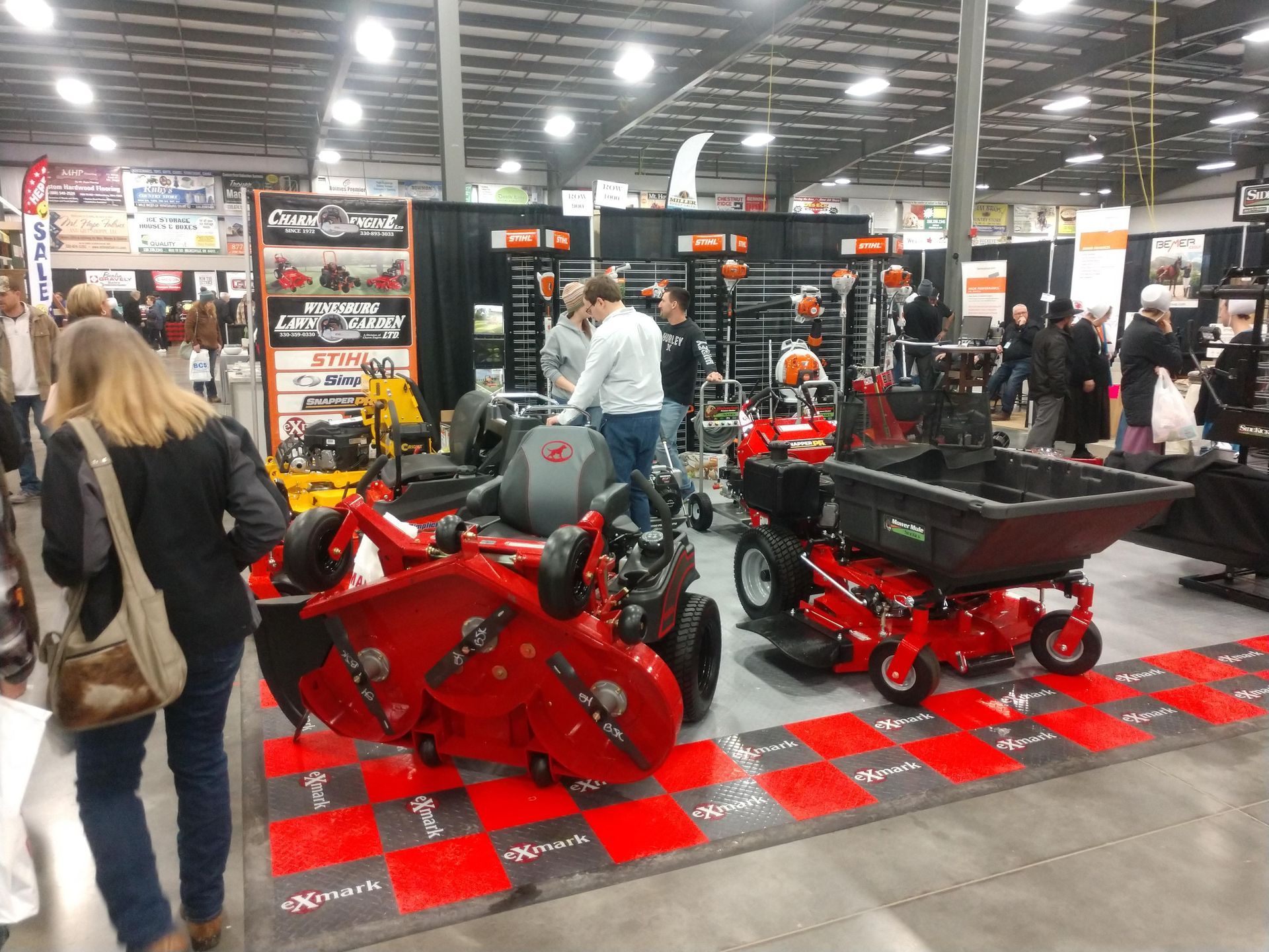 Indoor trade show booth displaying red lawn care equipment, with people browsing.