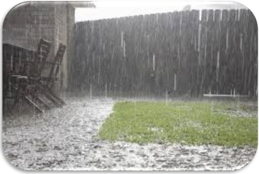 Rain pouring over a backyard patio and lawn, with water pooling on the ground.