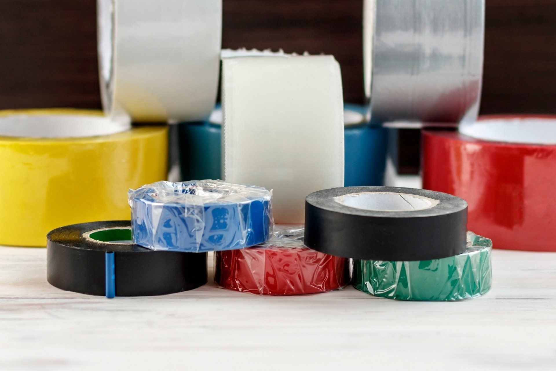Stacked rolls of colorful adhesive tape on a white surface, with large rolls in the background