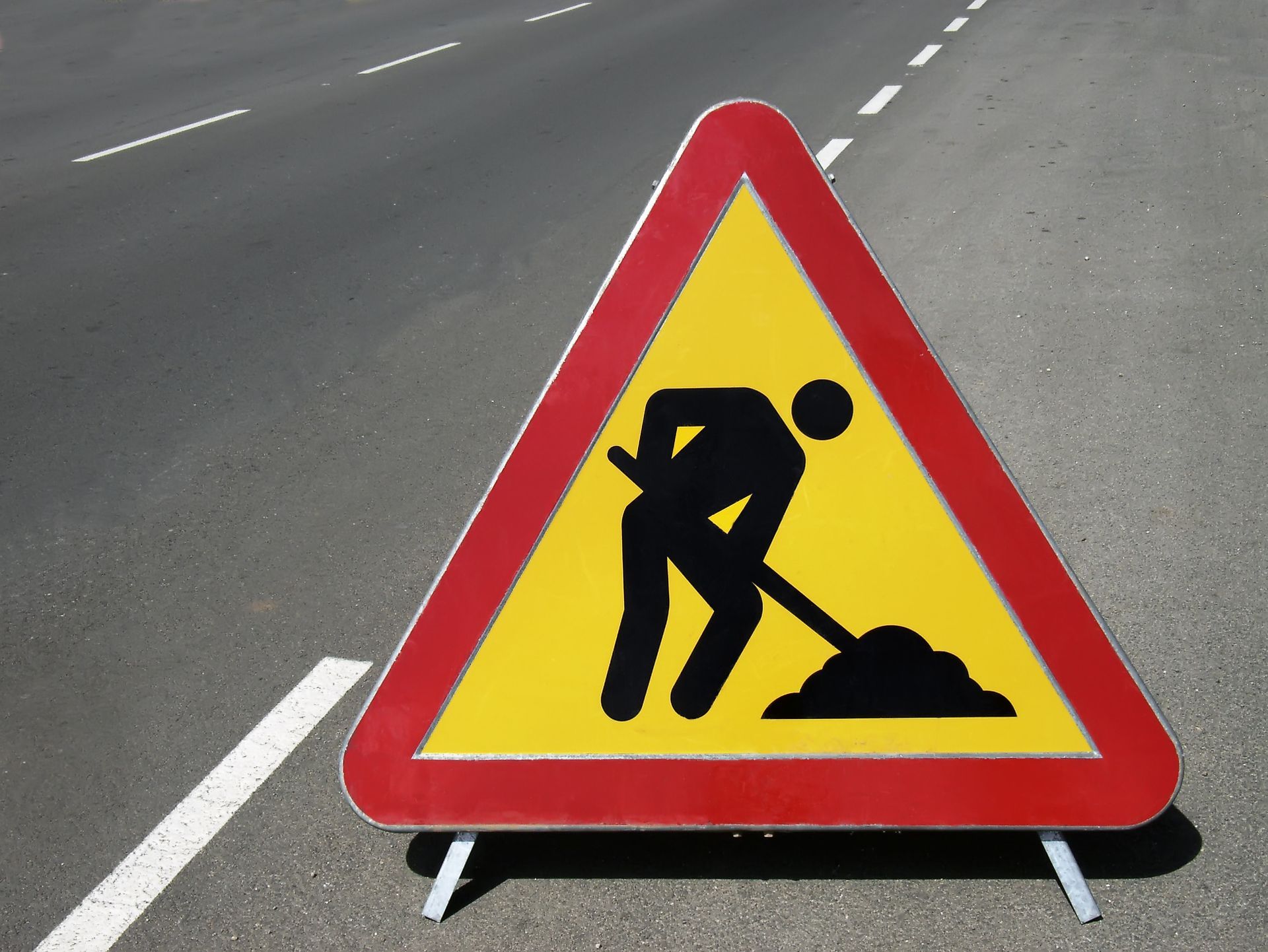 Roadwork warning sign with a worker digging on a red and yellow triangular stand on a road